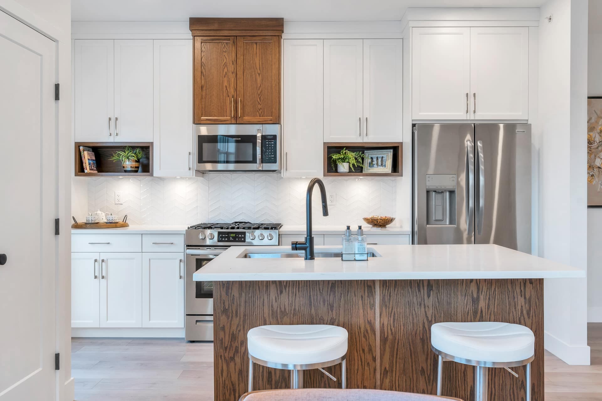 Osprey Ridge – Kitchen with white cabinetry, a wood accent cabinet over the range, stainless-steel appliances, and a wood island with white bar stools.