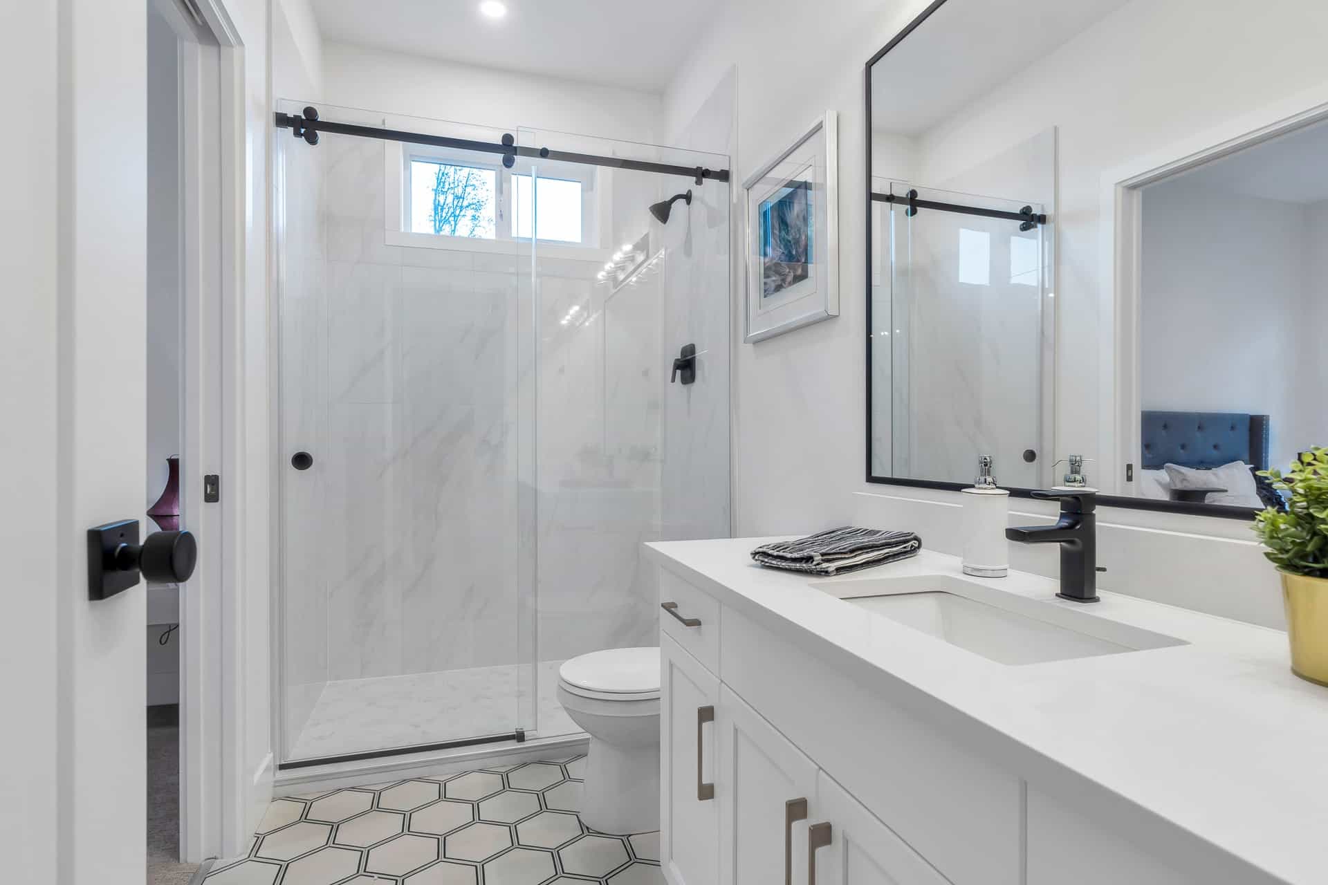 Osprey Ridge – Bathroom with a glass-enclosed shower, framed art, black fixtures, and a white vanity with a single sink.