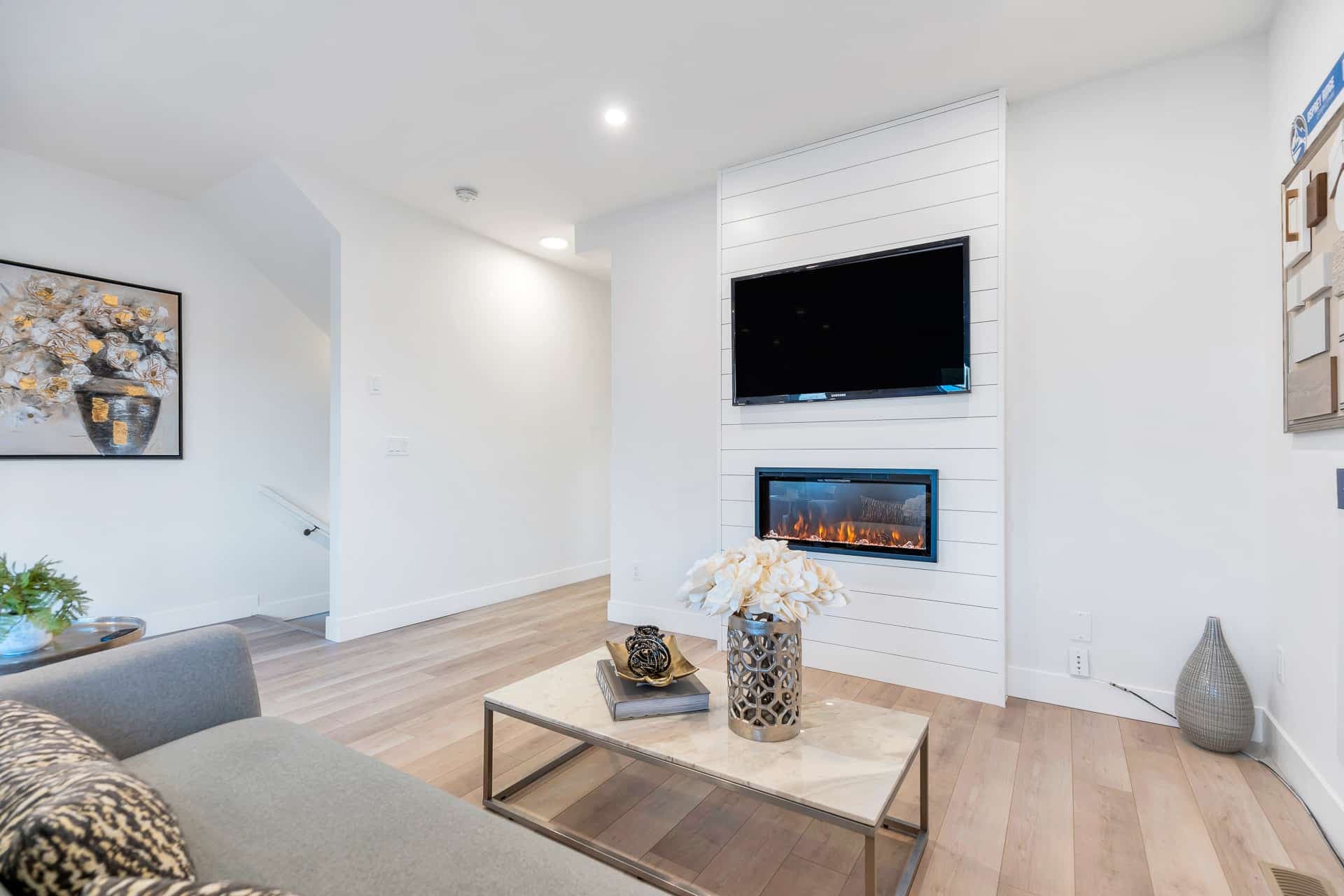 Osprey Ridge – Living room with a wall-mounted TV above a built-in electric fireplace, gray sofa, and marble coffee table with flowers.