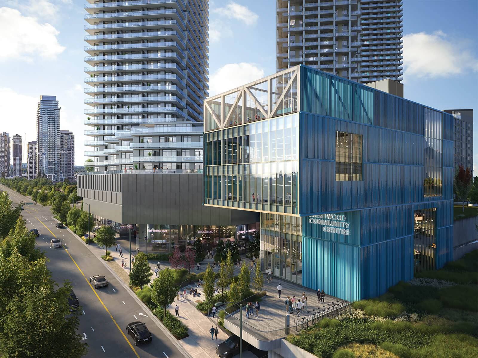 Brentwood Block – A modern blue multi-story community centre building with large glass windows stands beside high-rise residential towers along a tree-lined city street during a bright daylight afternoon. Pedestrians walk on paved plazas surrounding the building, while cars travel down the adjacent road against a distant city skyline under a clear blue sky.