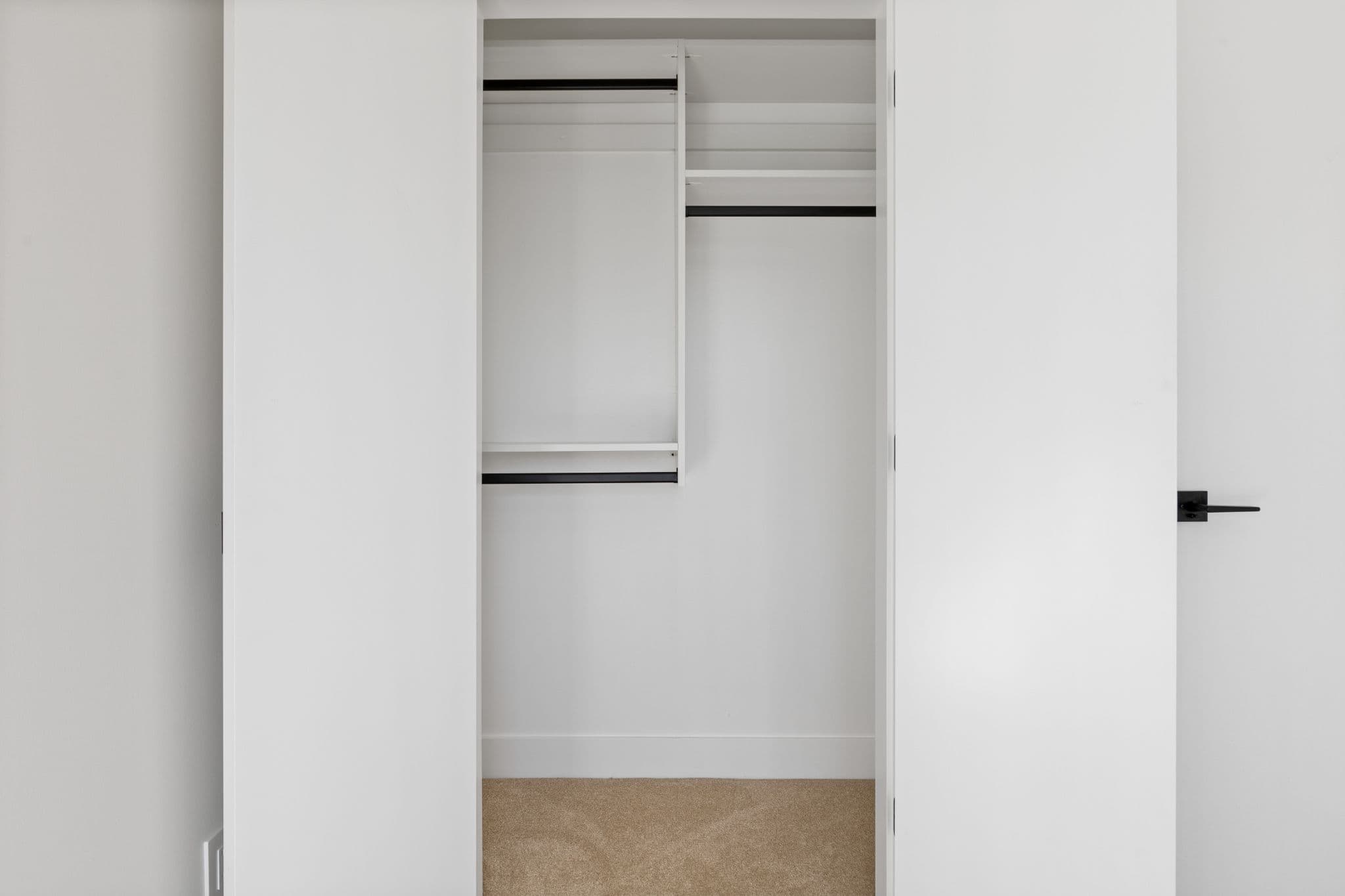Clearbrook Commons – Close-up view of an interior closet with built-in white shelving, hanging rods, and carpeted floor.
