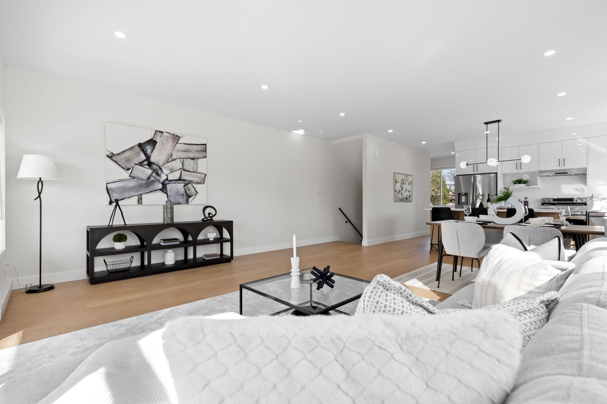 Clearbrook Commons – Open-concept living room featuring a white sectional sofa, glass coffee table, modern black console shelf, and adjoining kitchen.