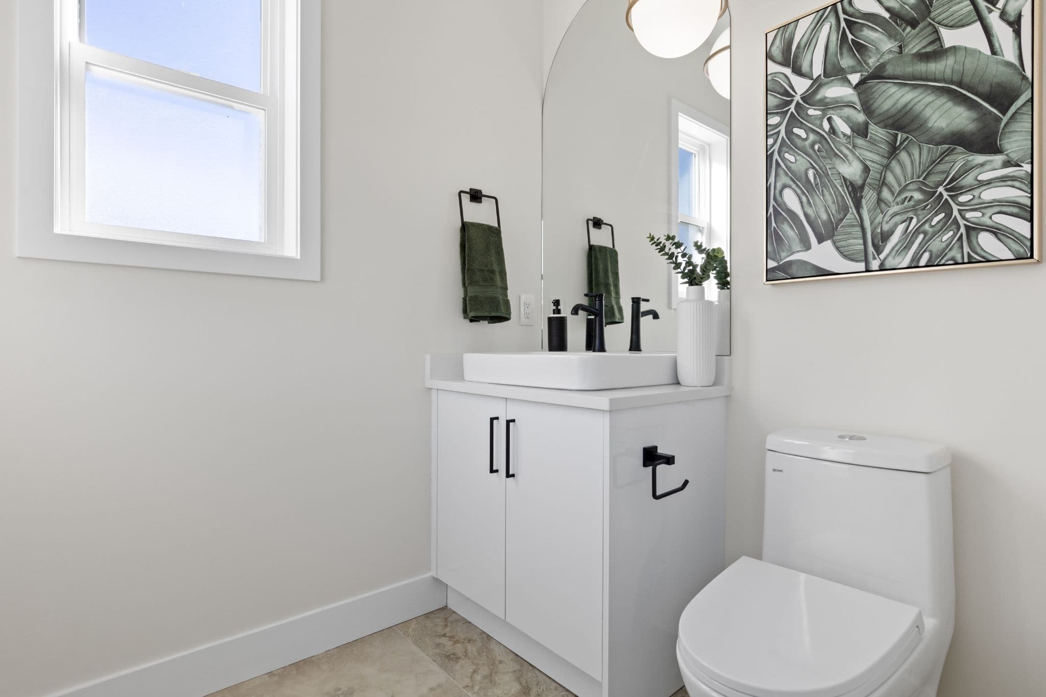 Clearbrook Commons – Powder room bathroom with white vanity cabinet, vessel sink, black plumbing fixtures, arched mirror, and toilet.