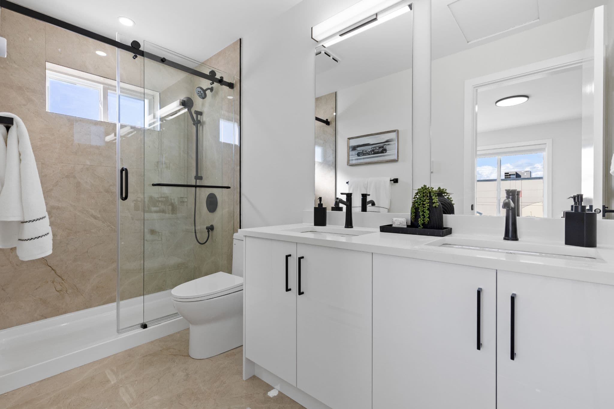 Clearbrook Commons – Bathroom featuring a white double-sink vanity, modern black hardware, large mirror, and glass sliding shower door.