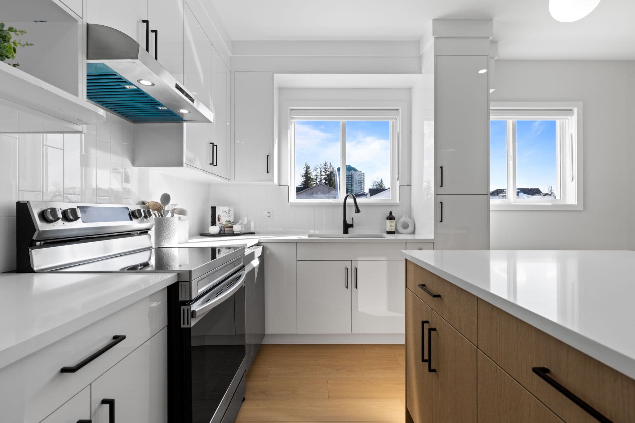 Clearbrook Commons – Kitchen detail with stainless steel range, range hood, white quartz countertops, white subway backsplash, and sink under a window.
