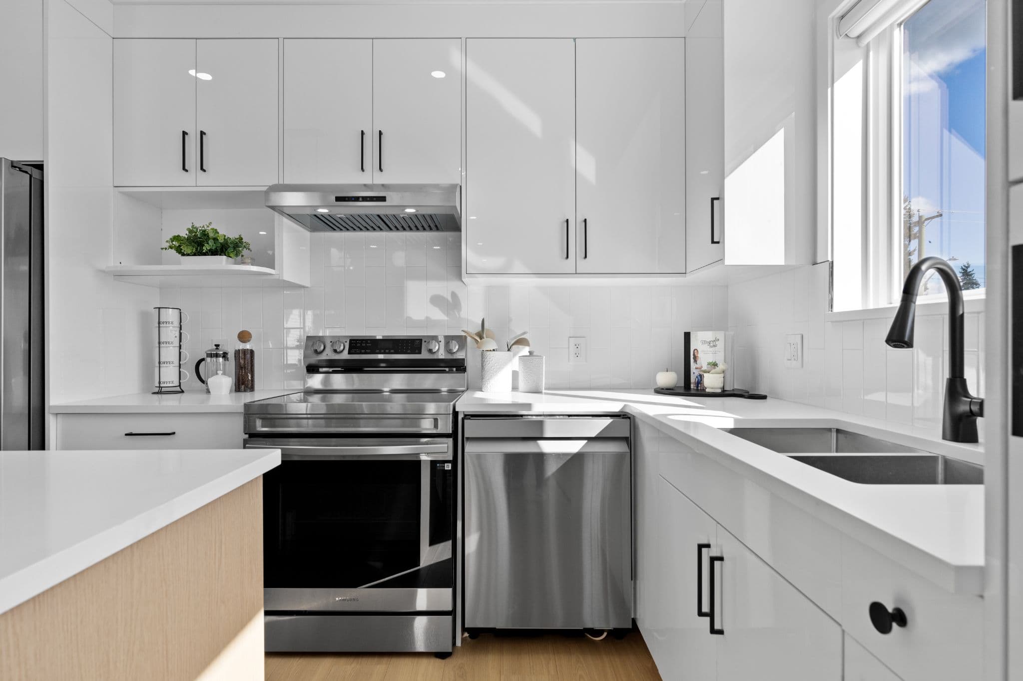 Clearbrook Commons – Kitchen counter workspace with stainless steel stove, range hood, dishwasher, and sink near window.