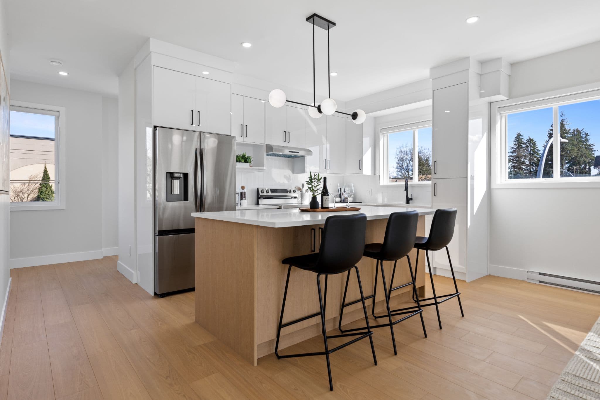 Clearbrook Commons – Kitchen area showing wood-faced island with black bar stools, stainless steel refrigerator, and white cabinetry.