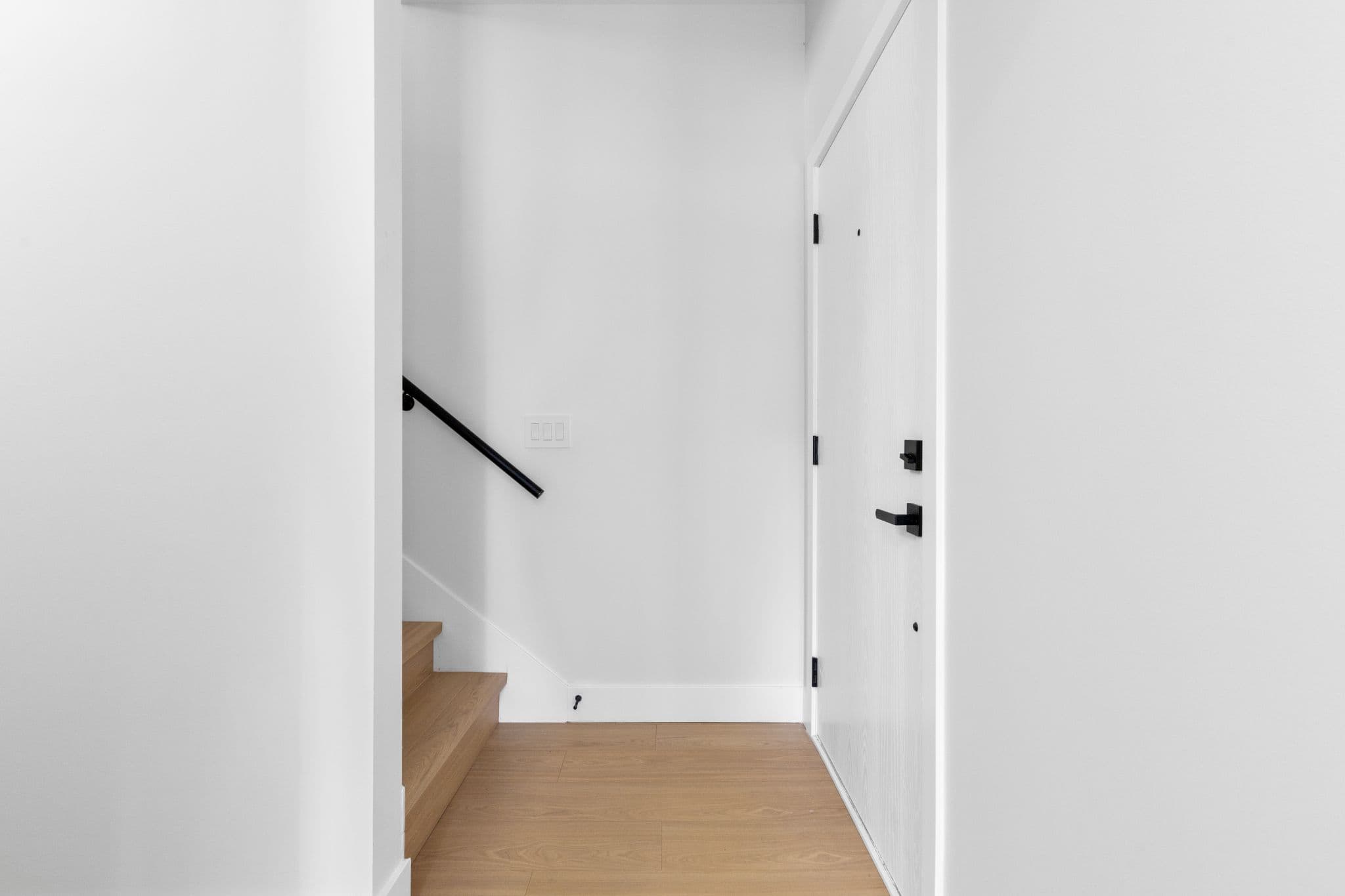 Clearbrook Commons – Entry foyer showing wood-look laminate flooring, white entrance door with black hardware, and stairs leading upward.
