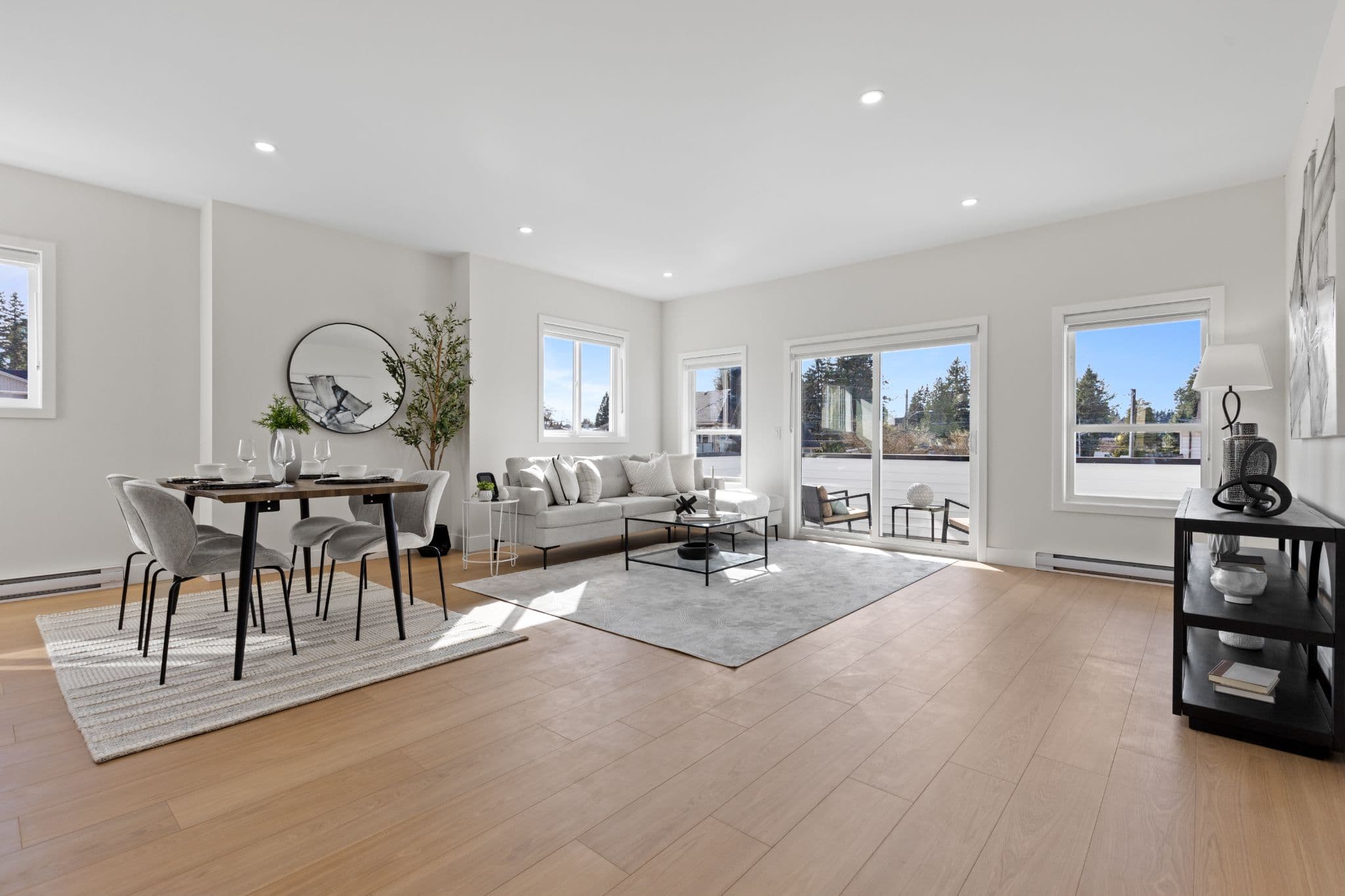 Clearbrook Commons – Main living room and dining area with soft grey sofa, coffee table, dining table, and sliding glass balcony door.