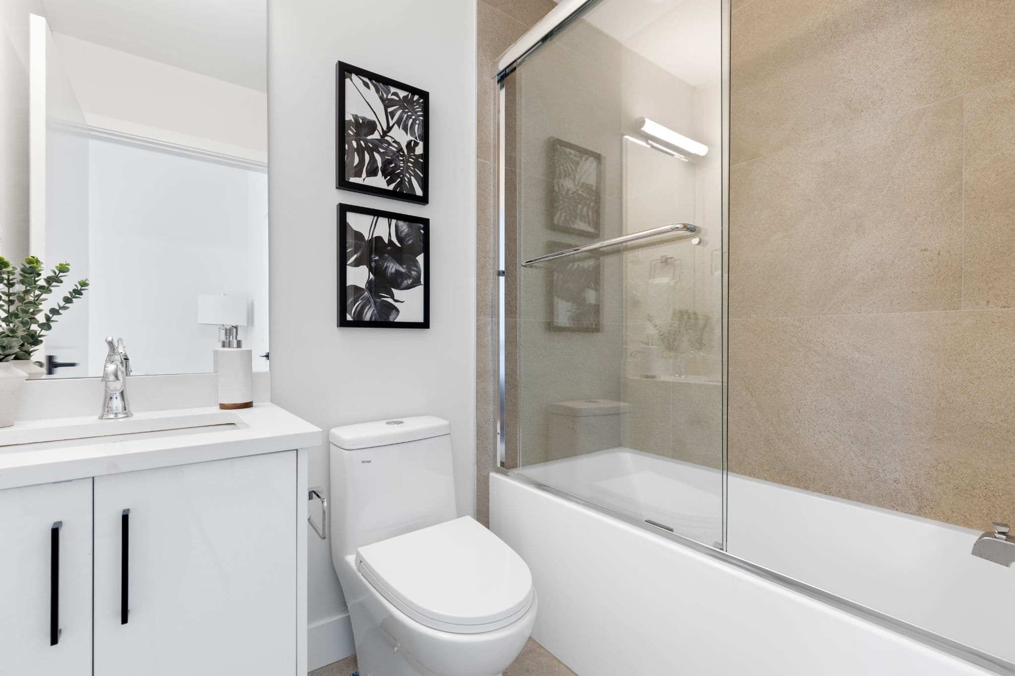 Clearbrook Commons – Full bathroom with white vanity cabinet, chrome faucet, toilet, and tiled bathtub with glass enclosure.