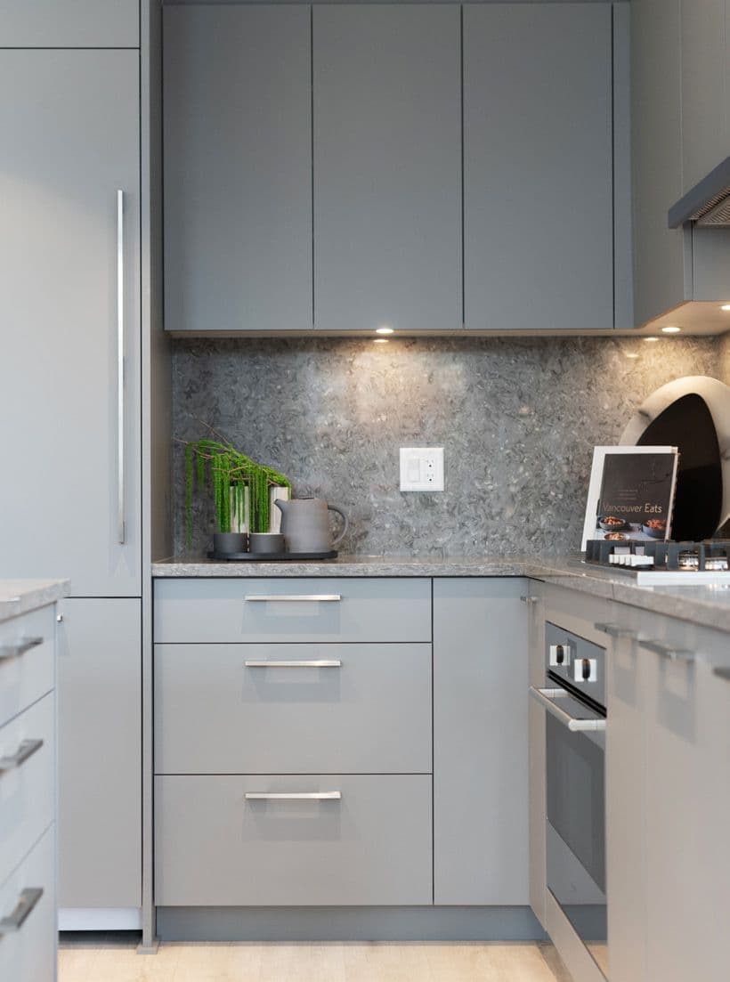 Perla Condos – A close-up of a grey kitchen with matching cabinetry, a stone backsplash, built-in oven, and small styling items on the counter.