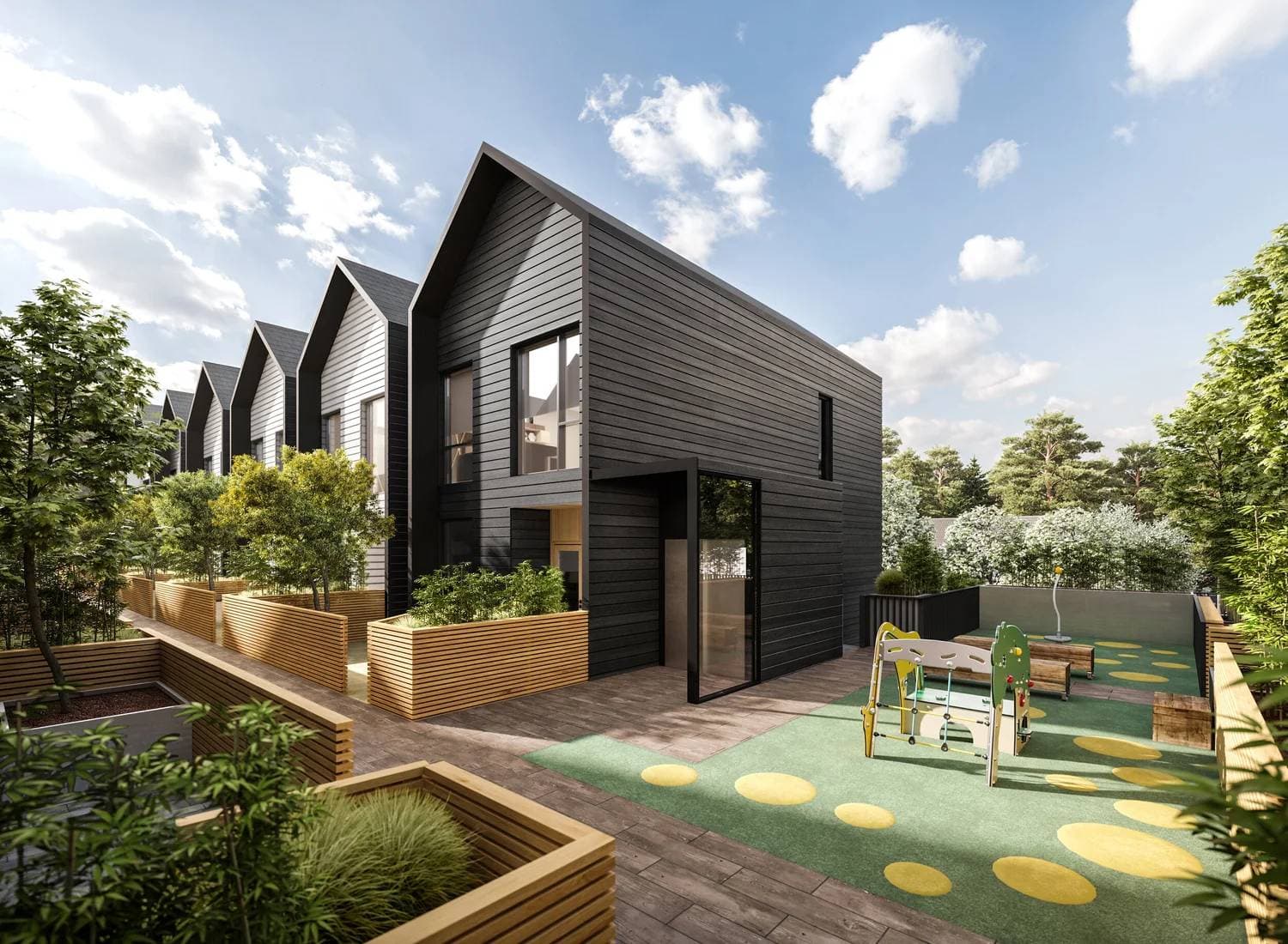Brighouse 22 – A row of modern gabled townhomes featuring dark charcoal and light siding, wooden planter boxes, and a children's play area with green padded turf. Set under a bright daytime sky with fluffy white clouds, the grounds are landscaped with young trees, wooden fencing, and lush greenery.