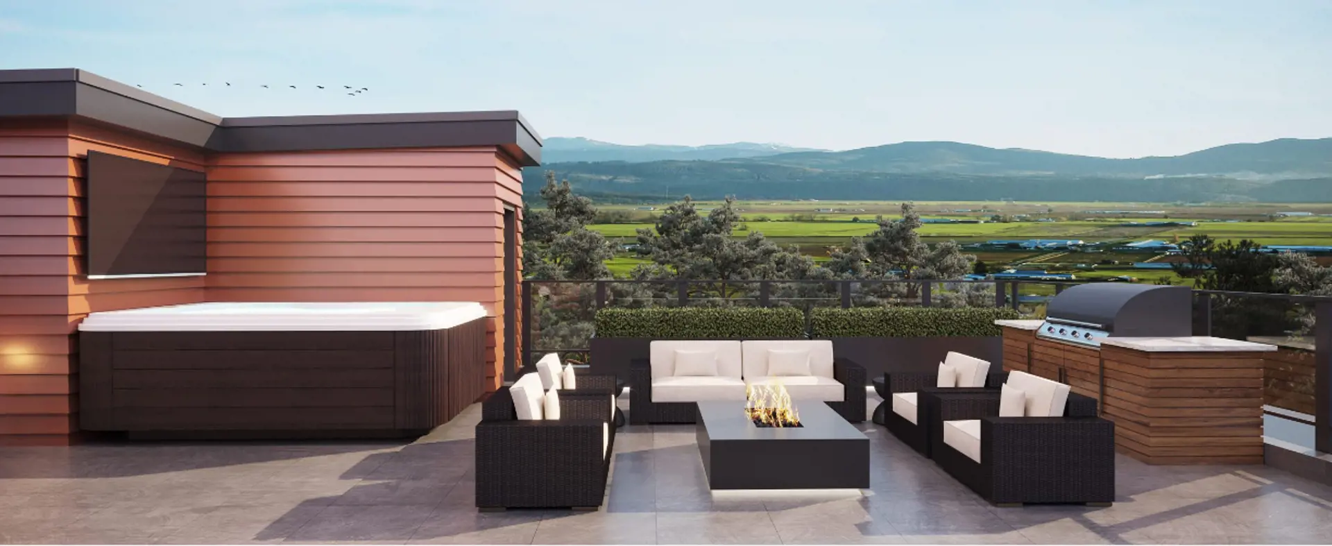 The Peak at Mountain View – Rooftop deck with a hot tub, outdoor sofas around a fire pit table, and a built-in barbecue, overlooking farmland and mountains.