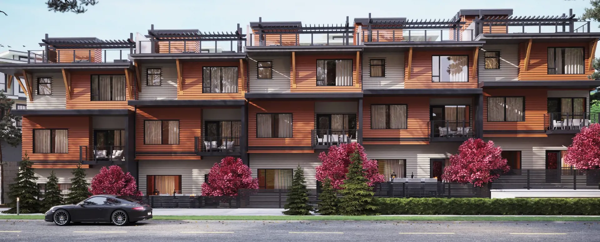 The Peak at Mountain View – Street-level view of a row of three-story townhomes with orange and grey siding, rooftop pergolas, and flowering pink trees along the sidewalk.