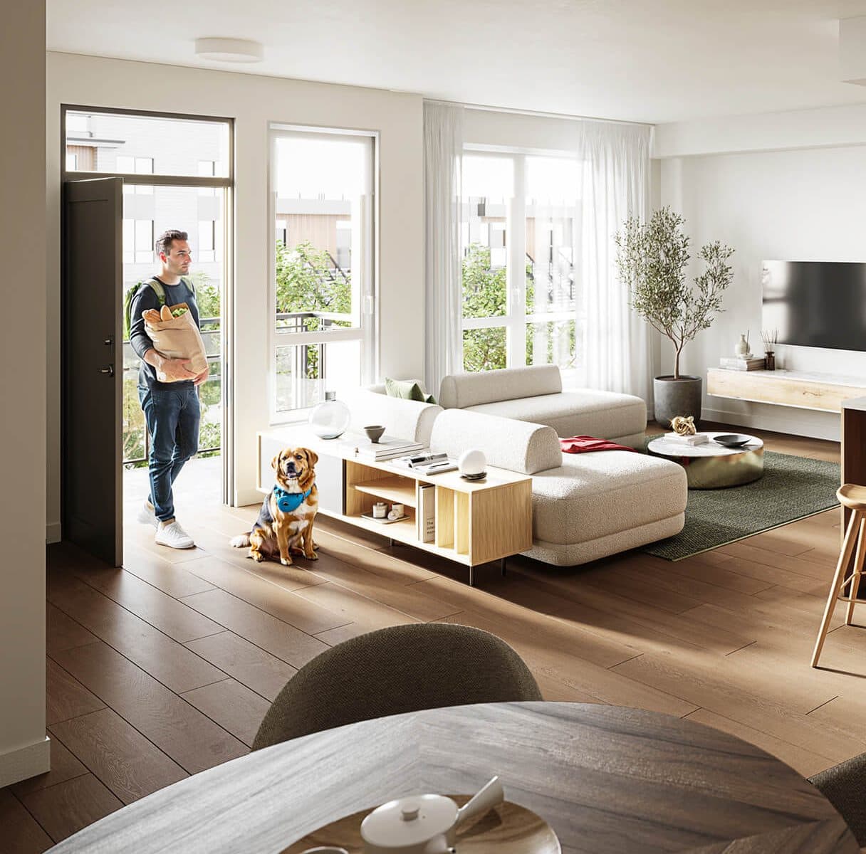 Kestrel – Open-concept living room with a man carrying groceries and a dog seated near a beige sectional, large windows overlooking neighboring townhomes.
