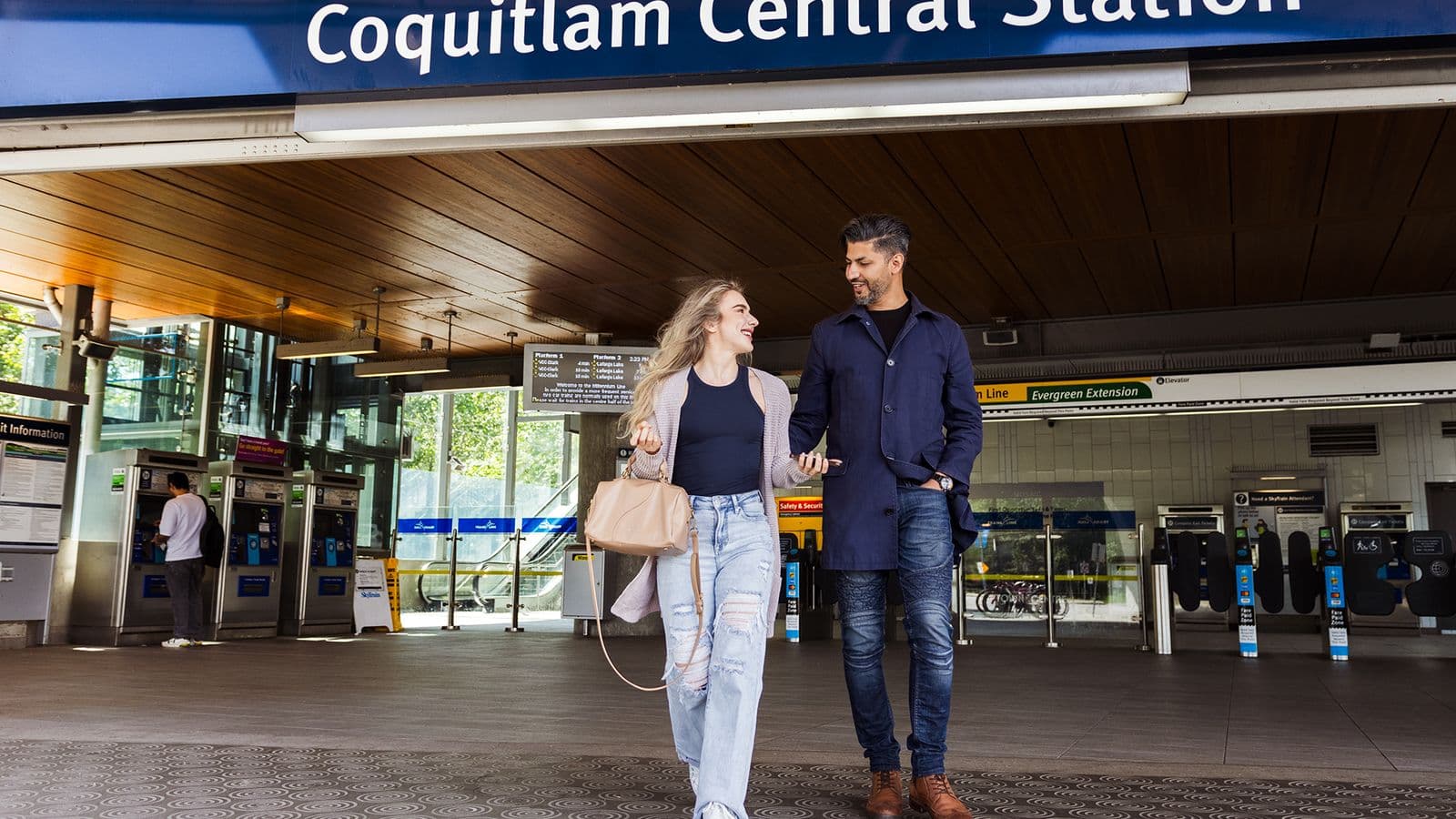 Kestrel – Lifestyle photo of a couple walking outside Coquitlam Central SkyTrain station, showing nearby transit access rather than the building itself.