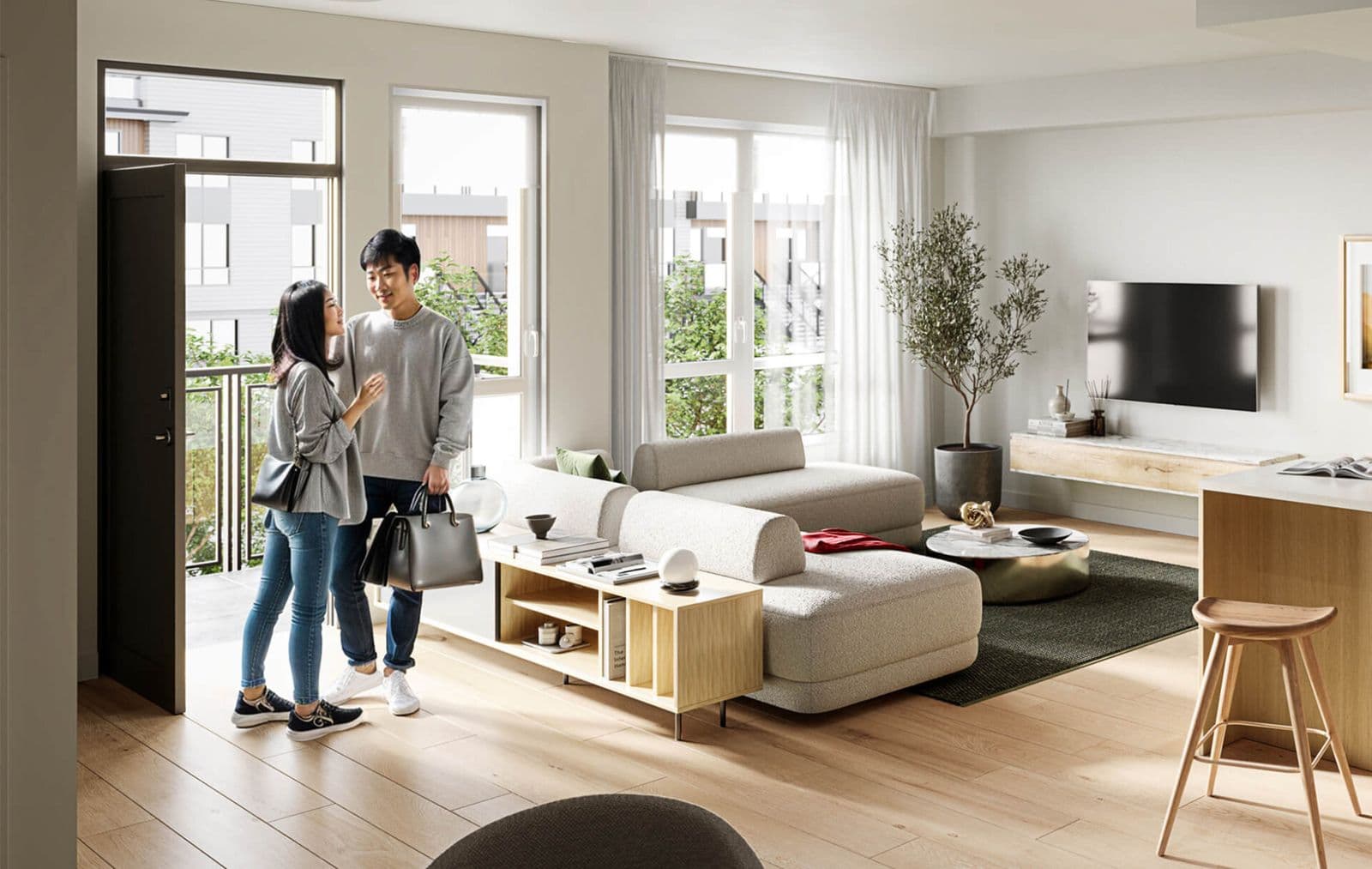 Kestrel – Living room with a couple standing near an open balcony door, beige sectional sofa, wall-mounted TV and a potted olive tree.