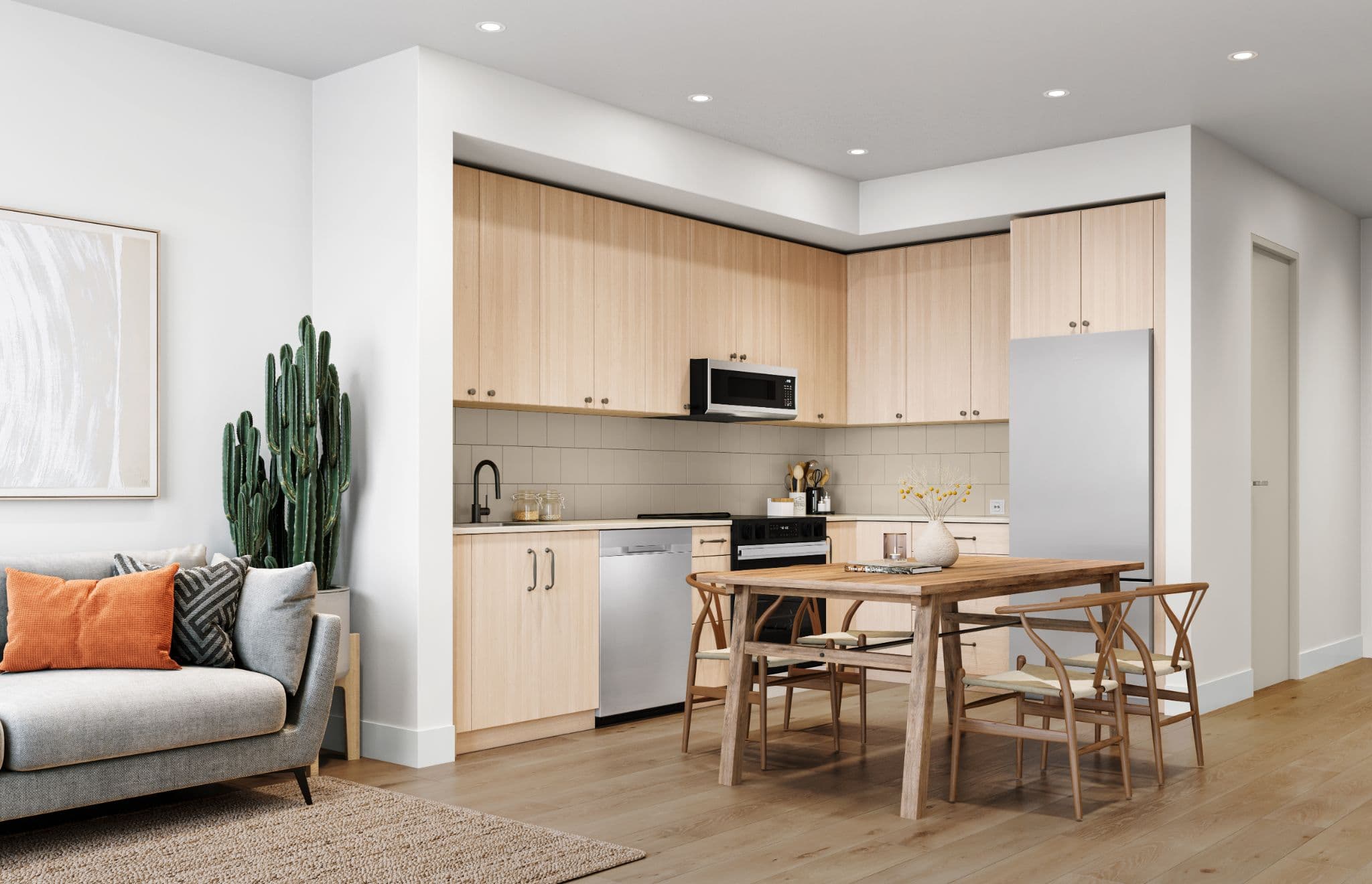 Auburn – Open-concept unit interior with light wood kitchen cabinets, stainless appliances, a wooden dining table, and a grey sofa with a cactus plant.