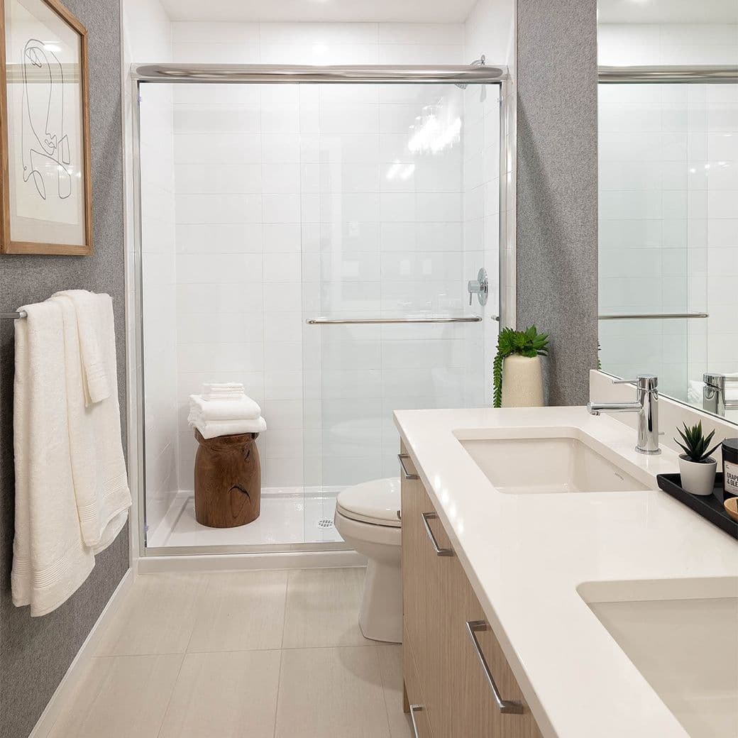 Southaven – Bathroom with a glass-enclosed walk-in shower, toilet, and a white double vanity with wood-tone cabinet fronts.
