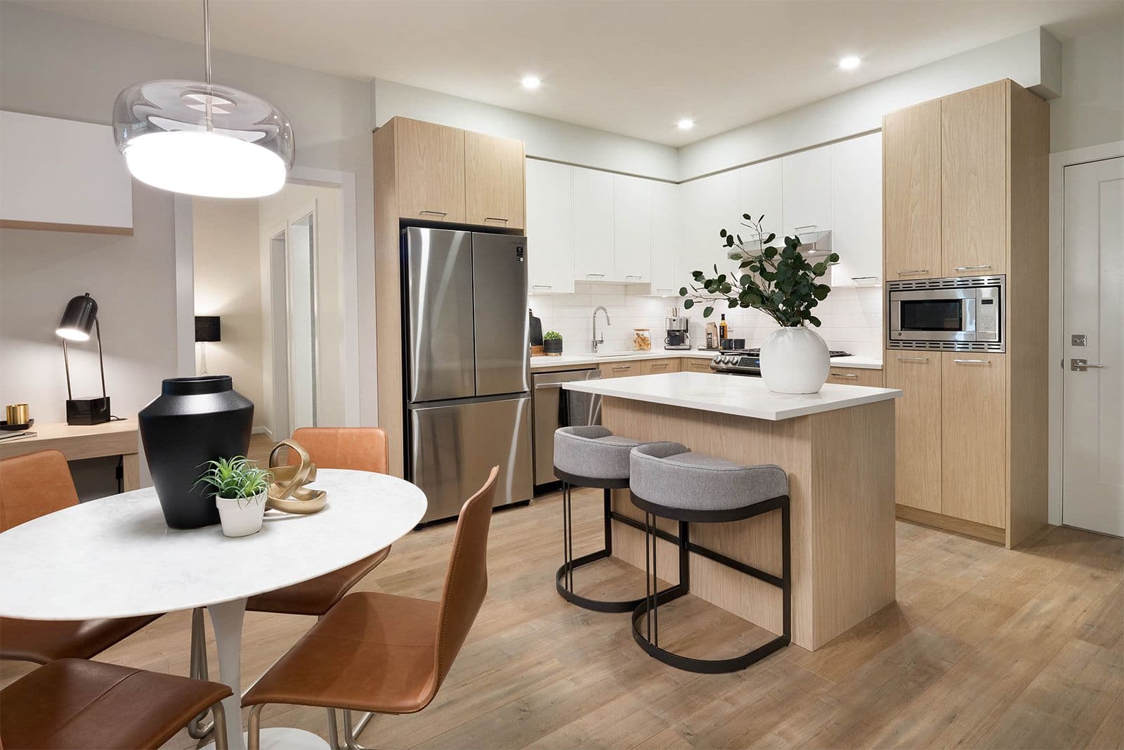 Southaven – Kitchen with light wood and white cabinetry, stainless fridge and microwave, an island with gray stools, and a round dining table with orange chairs.