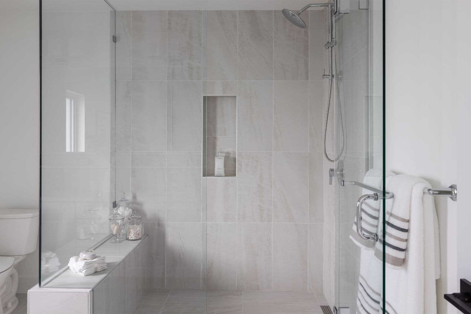 Brighton North – Modern walk-in shower with glass enclosure, wall-to-wall light marble-look tiles, shower niche, and a bench.