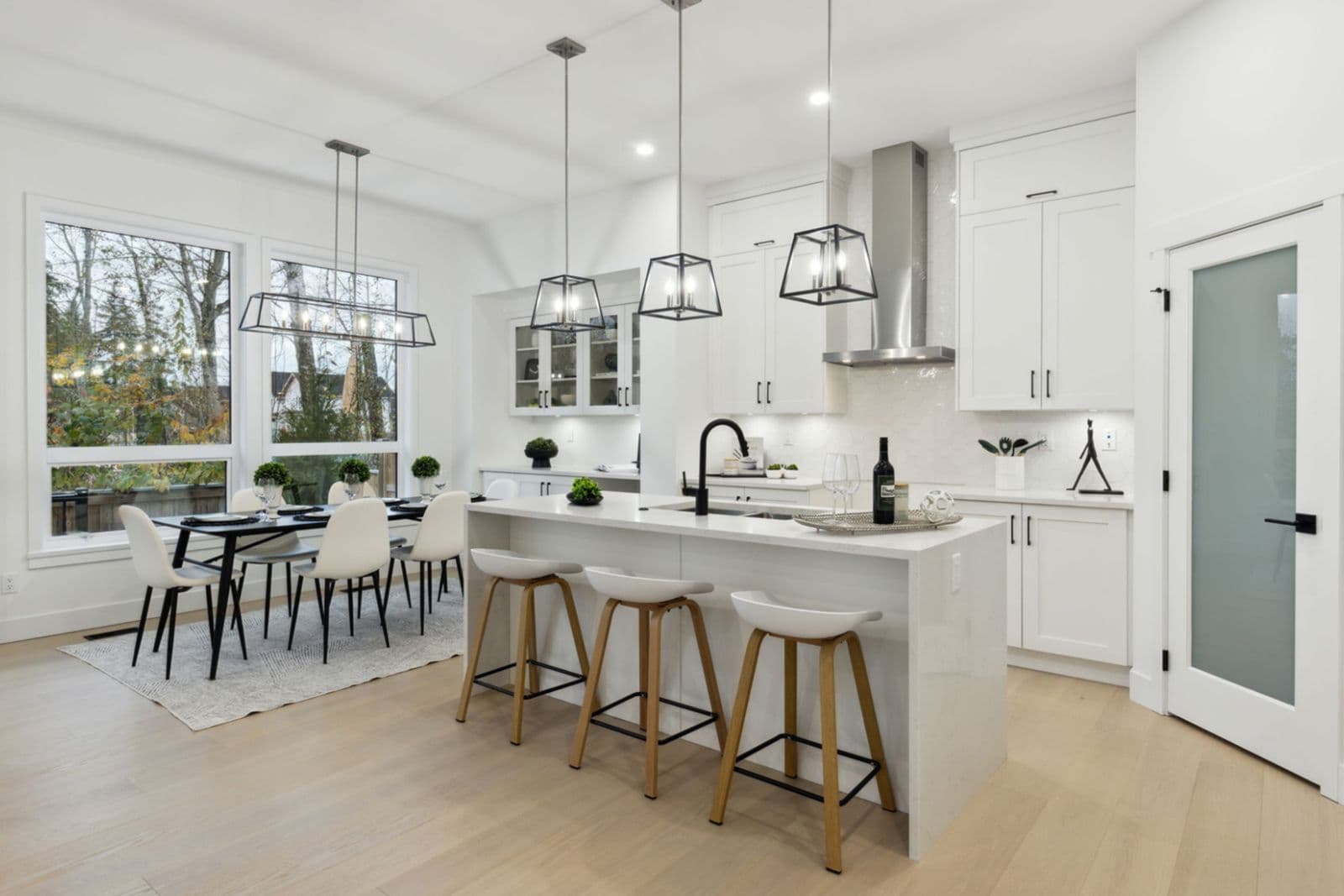 Brighton North – Open-concept kitchen and dining area featuring a kitchen island with stool seating, pendant light fixtures, white cabinetry, and large windows.