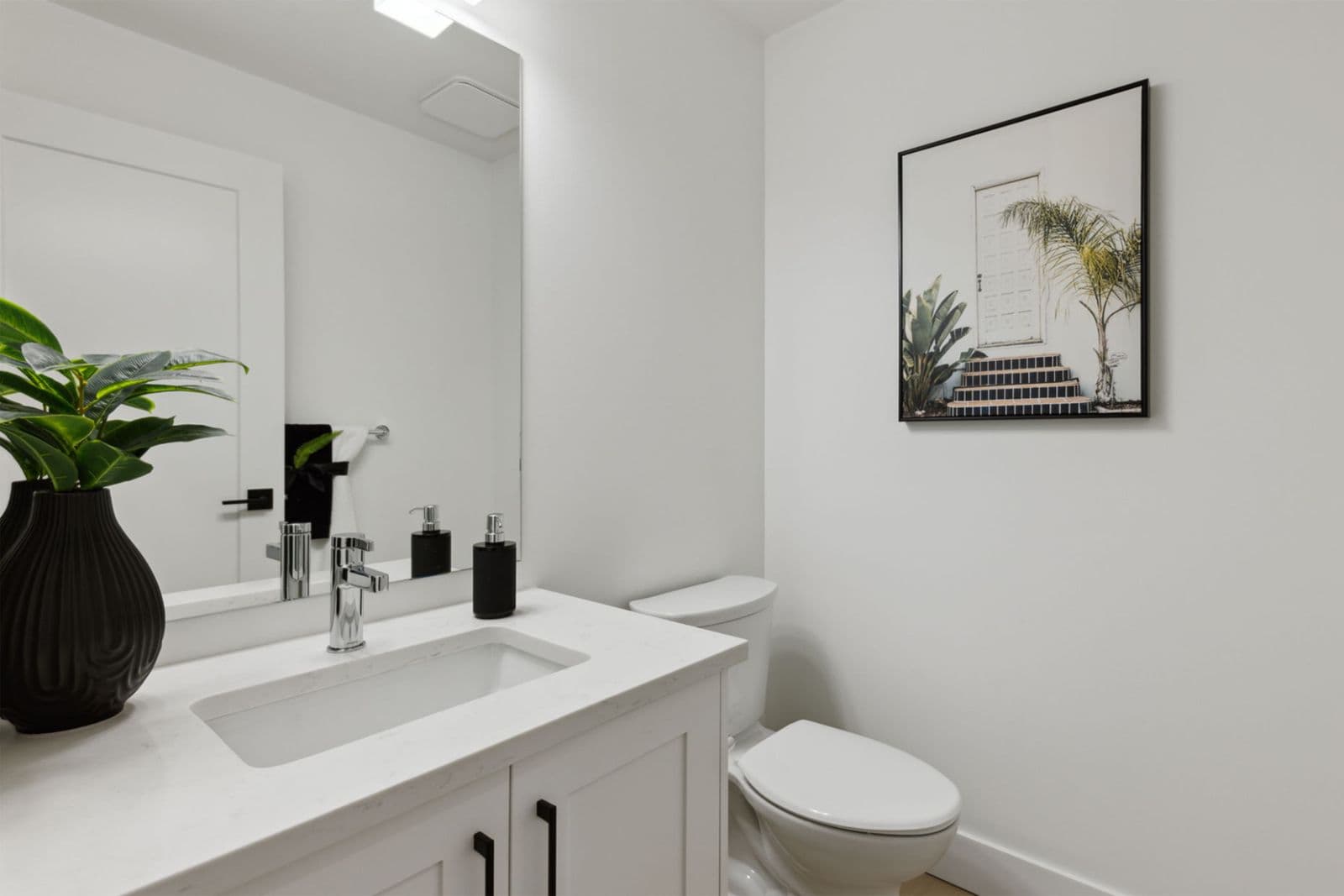 Brighton North – Powder room featuring a white vanity with quartz countertop, chrome faucet, mirror, toilet, and decorative wall art.