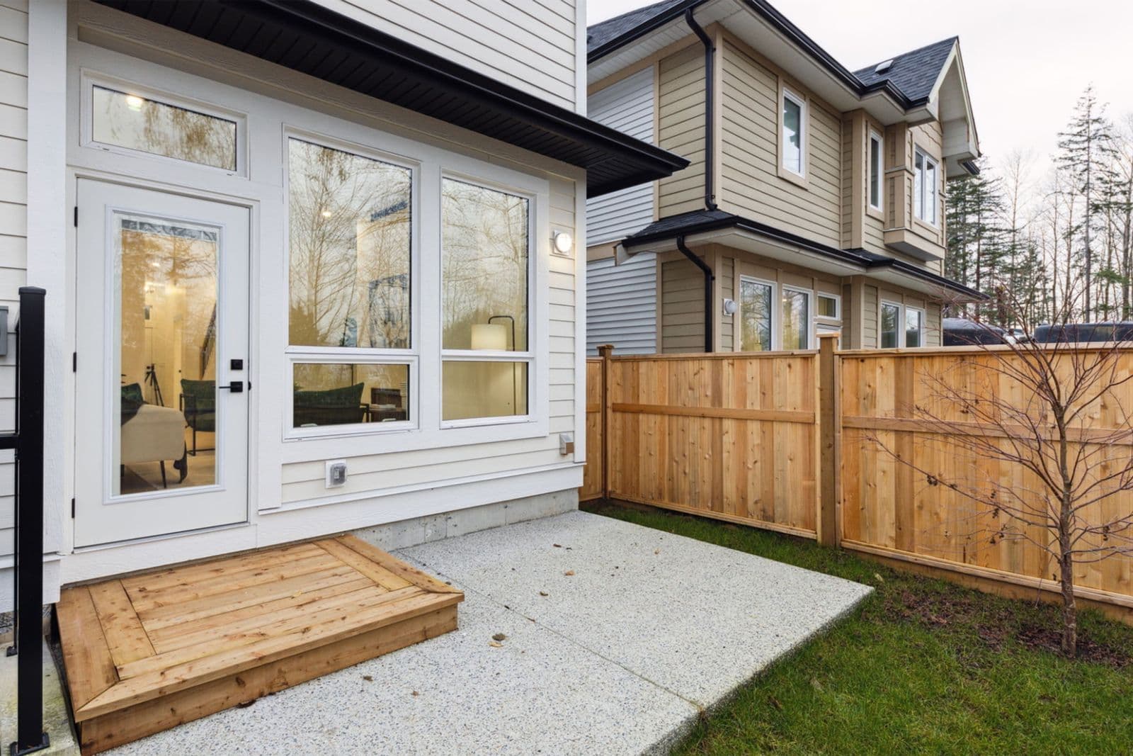 Brighton North – Rear patio and backyard area of a townhome with concrete slab, wooden steps, side fencing, and exterior siding details.