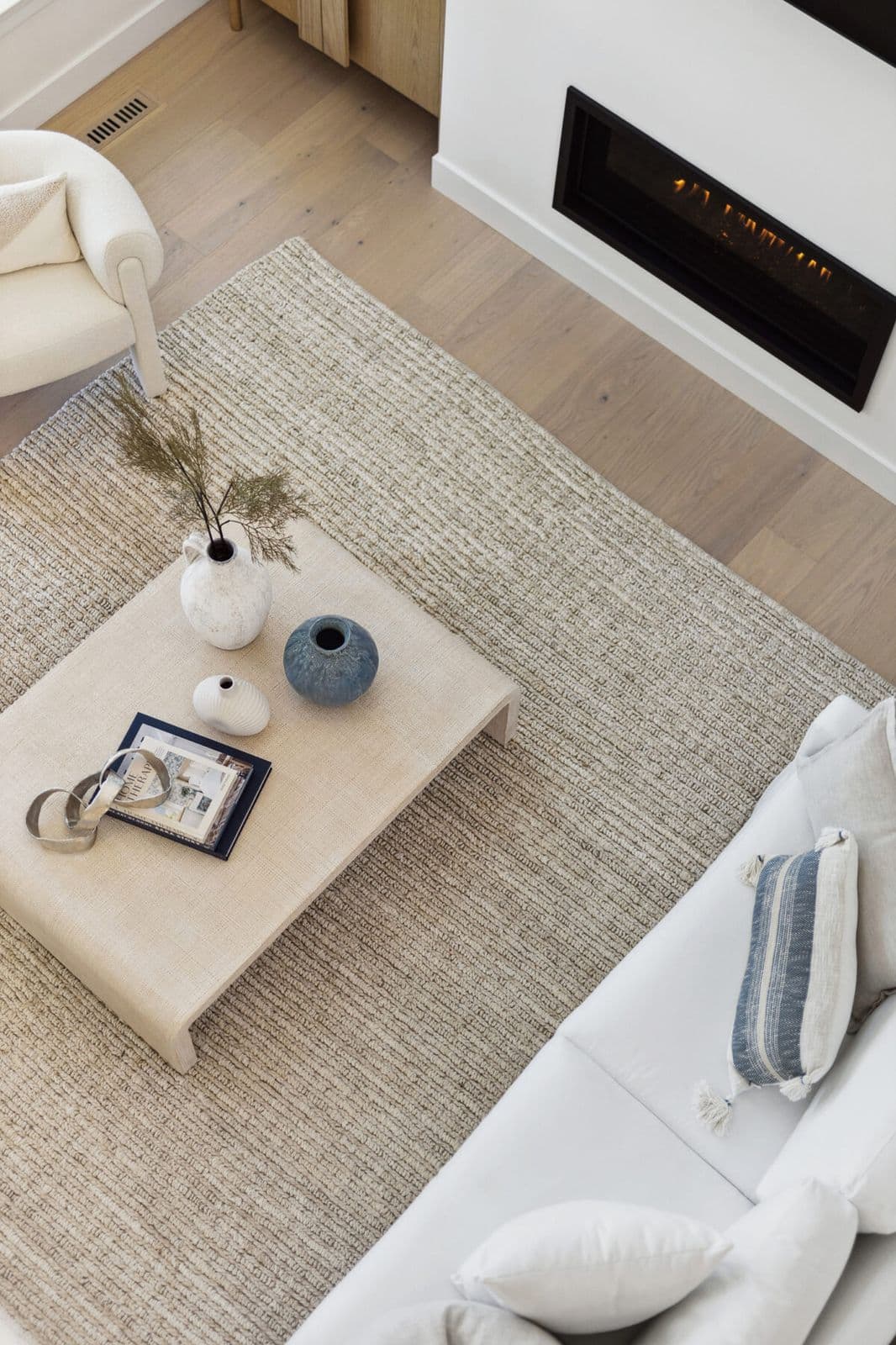 Brighton North – Overhead view of a living room setup showing a coffee table with decorative vases, textured area rug, sofa, and electric fireplace.