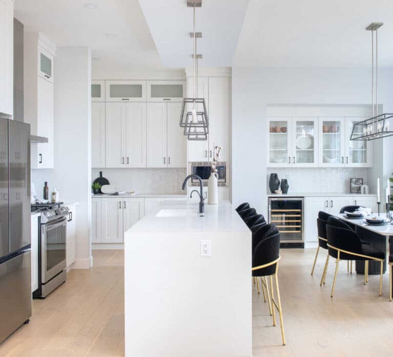 Brighton North – Bright kitchen featuring a large waterfall island with black barstools, stainless steel appliances, built-in cabinetry, and adjacent dining area.