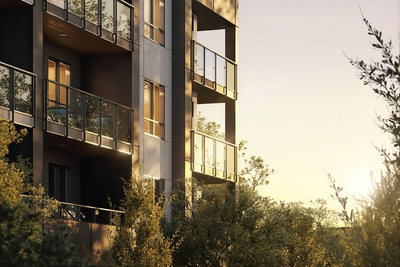 Harrison – A close-up architectural view of a modern multi-story residential building featuring sleek dark cladding, warm wood soffits, and glass-railed balconies. Soft golden sunlight bathes the facade, casting long shadows through the lush green trees surrounding the structure.