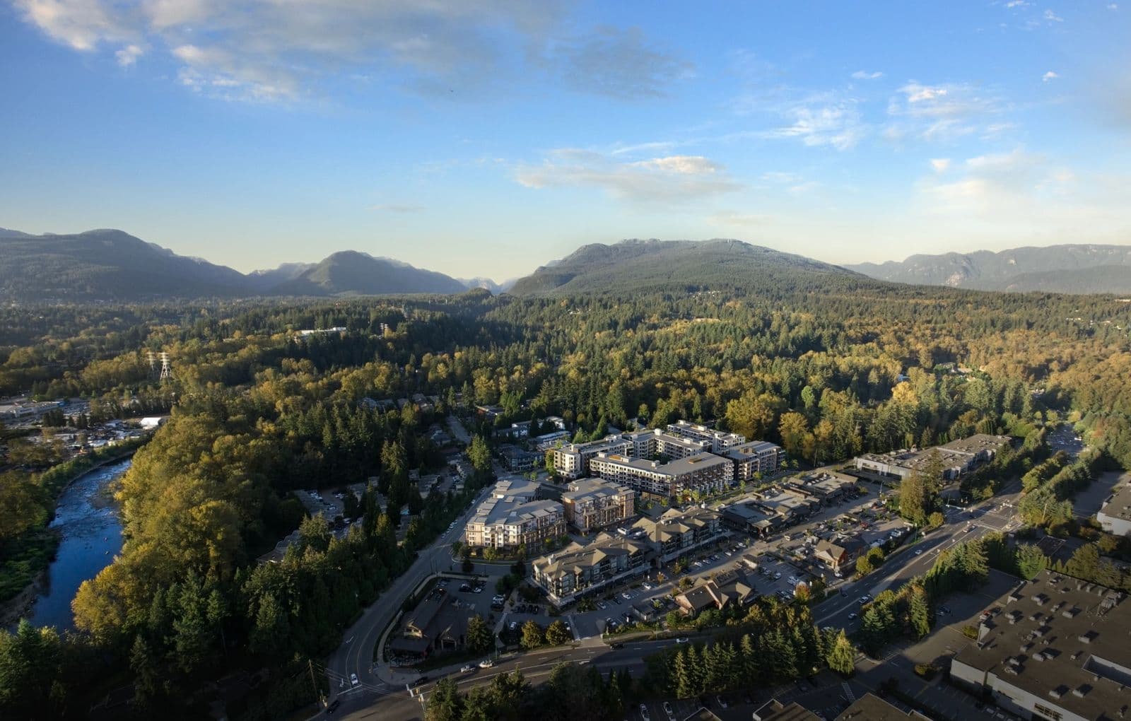 Maplewood Gardens – Aerial view of a mixed-use development site surrounded by forest, with a river and mountains in the background.