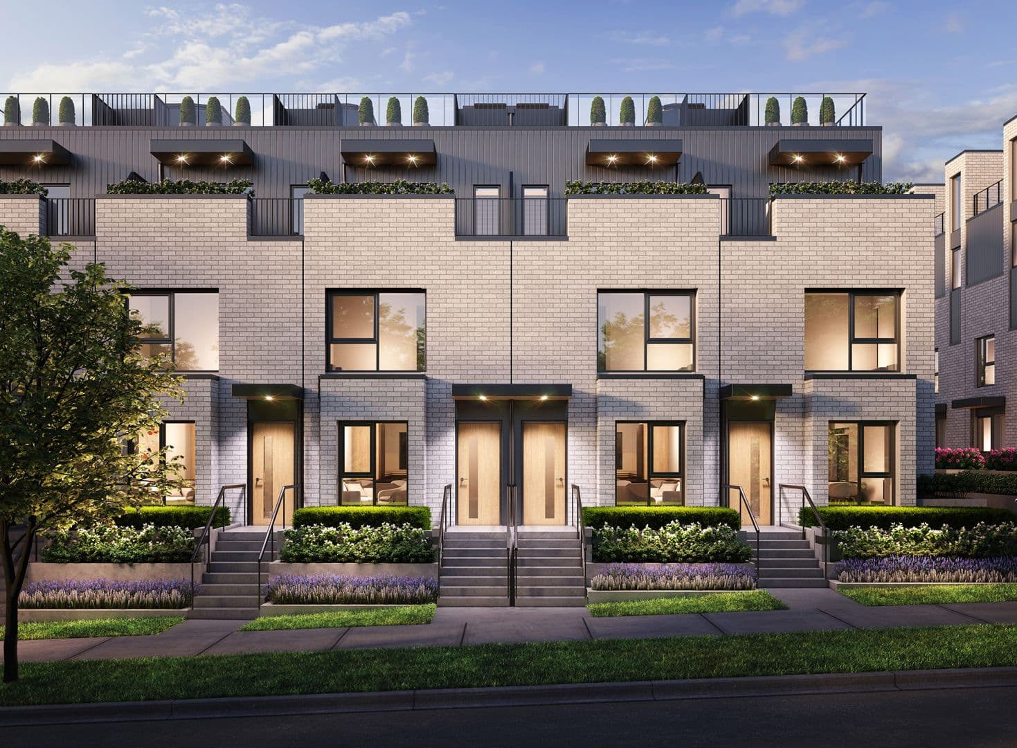 Grace – Row of light brick three-story townhomes at dusk with rooftop terraces, wood front doors, and landscaped front gardens with lavender planting.
