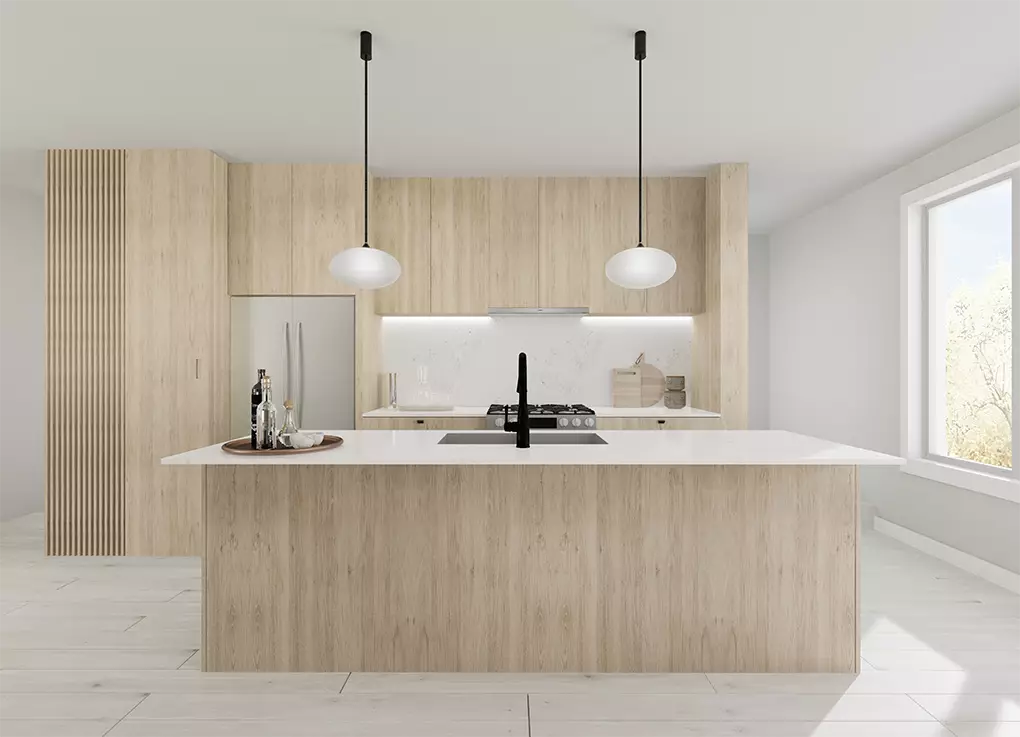 Uptown Cedar – A modern, minimalist kitchen featuring light wood cabinetry with a vertical slatted detail, white solid-surface countertops, and an integrated stainless steel refrigerator and gas cooktop. A large kitchen island with an undermount sink and matte black faucet sits in the foreground beneath two hanging oval pendant lights, with bright natural light streaming in from a side window.