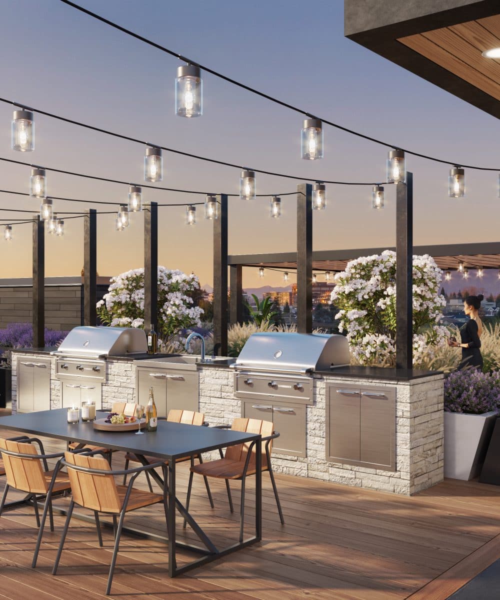 Pure West 49 – Rooftop amenity deck at dusk with an outdoor BBQ kitchen, dining table, and string lights overlooking the city.