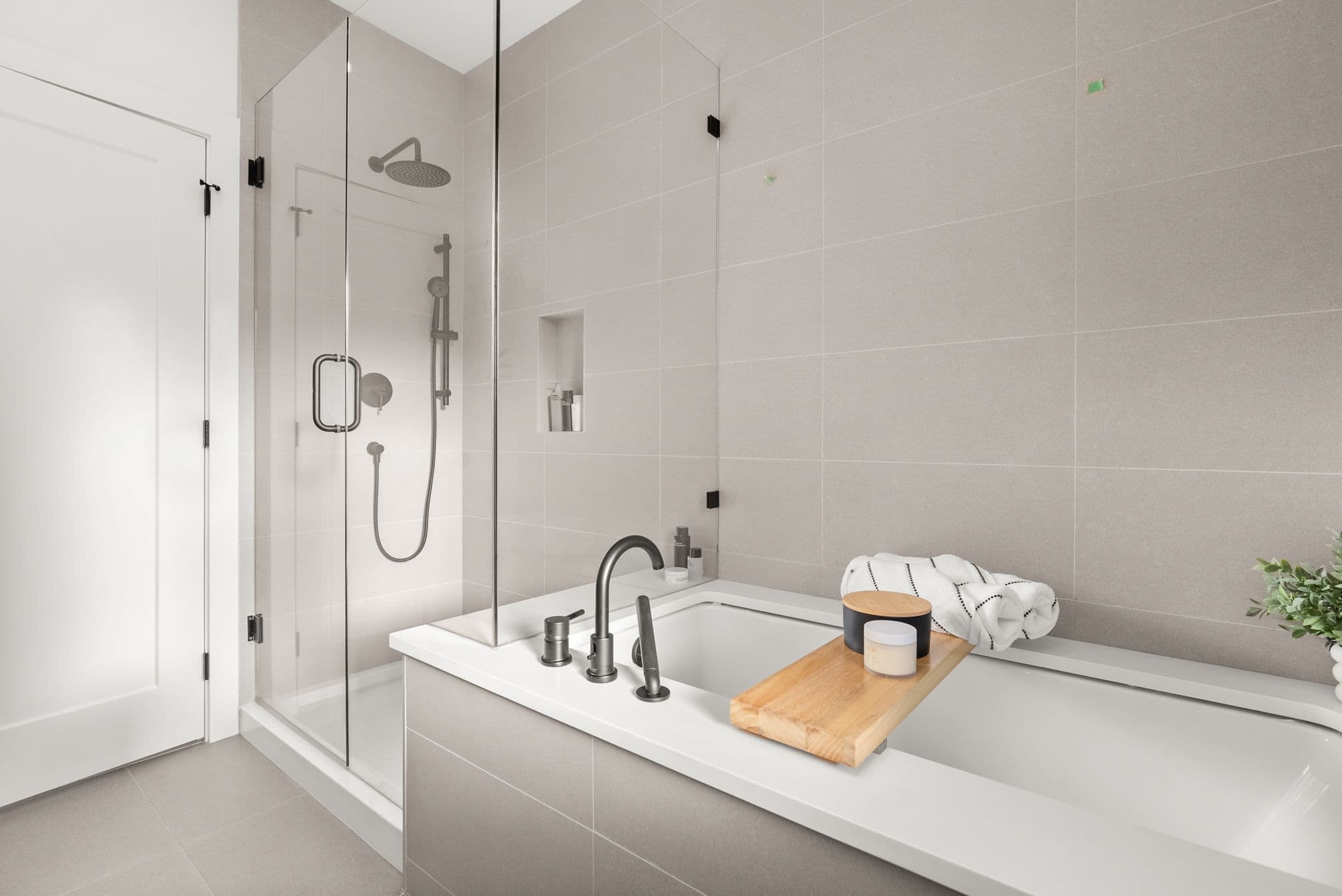 Ebor Plateau – A modern bathroom featuring a white drop-in soaking tub with dark matte plumbing fixtures alongside a glass-enclosed walk-in shower. Neutral beige wall tiles, a built-in shower niche, and a wooden bath caddy with spa accessories create a serene, minimalist atmosphere.
