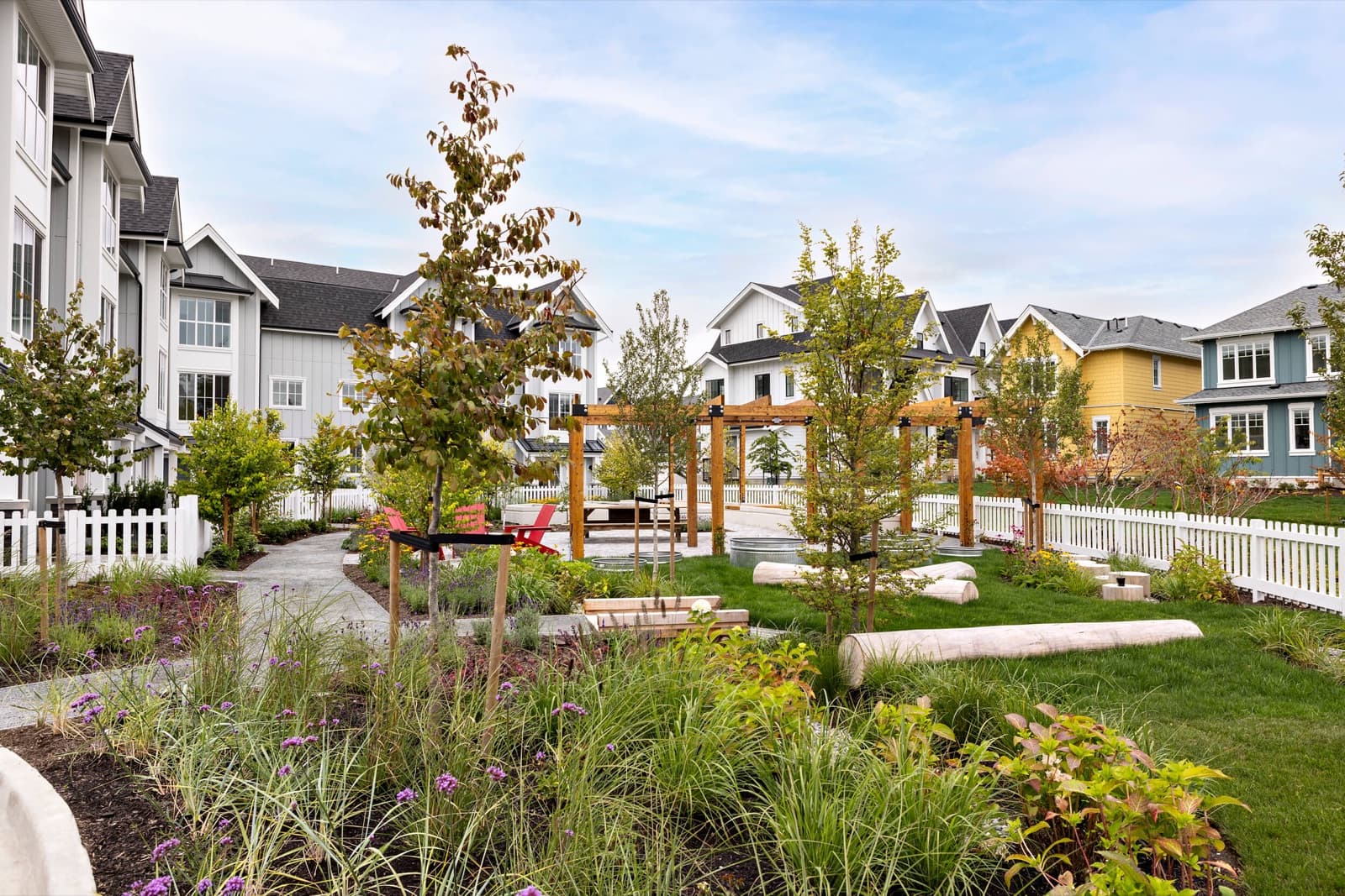 Southlands Tsawwassen – Shared community green space with wooden pergolas, red adirondack chairs, log benches, and a mix of colorful townhomes surrounding the lawn.