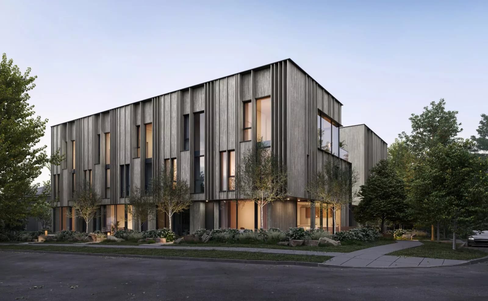 Ash 28 Condos – Rendering of a three-storey building with vertical wood-slat siding surrounded by mature trees, showing the corner of the structure at dusk.