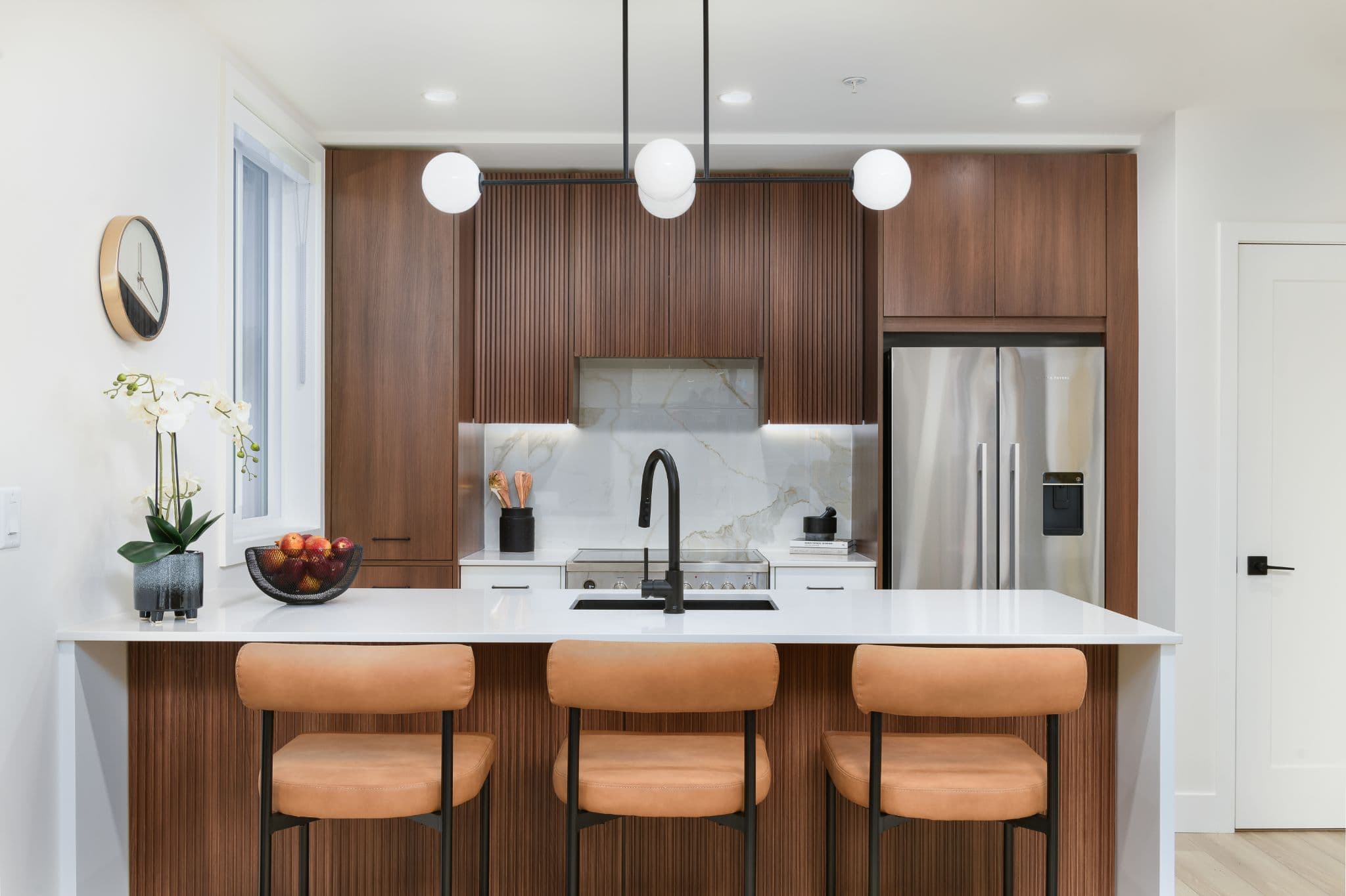 Aria 2 – Kitchen with dark wood cabinetry, a marble backsplash, globe pendant lights, and a stainless steel refrigerator.