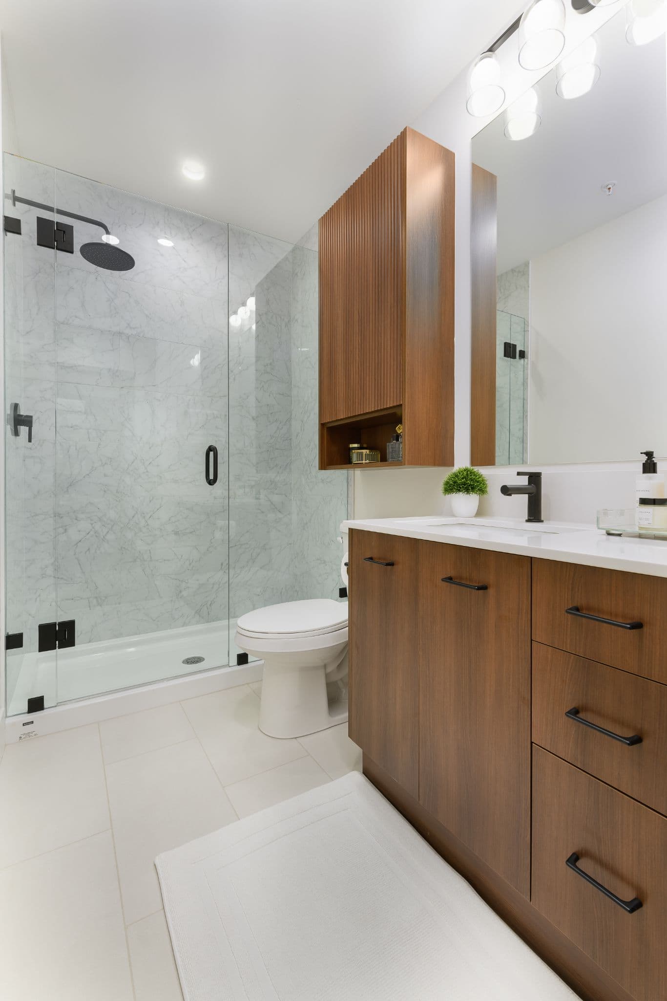 Aria 2 – Bathroom with a glass-enclosed shower with marble tile, black fixtures, a toilet, and a wood vanity with double sinks.