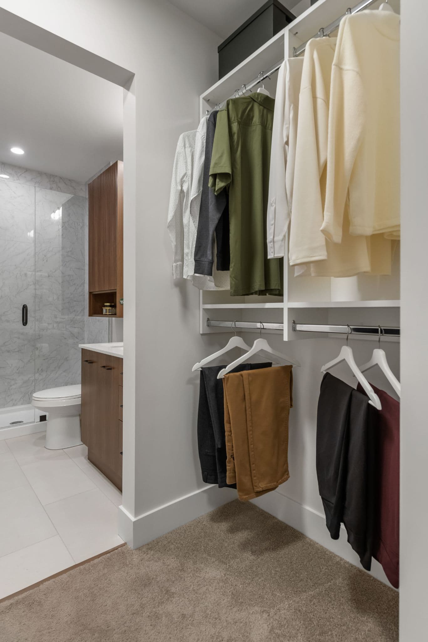 Aria 2 – Walk-in closet with clothes hanging on rods, opening into an ensuite bathroom with a marble shower and vanity.