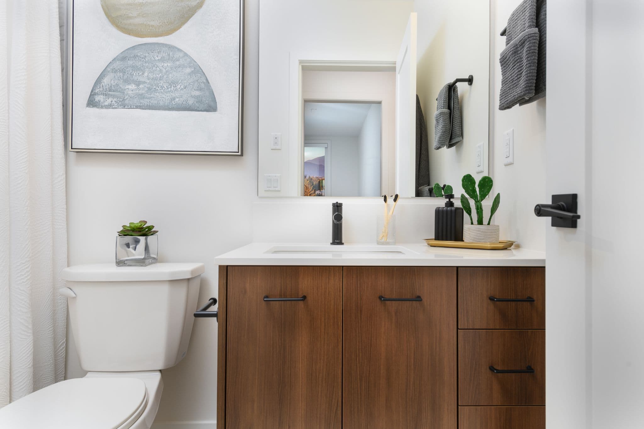Aria 2 – Bathroom vanity with dark wood cabinets, black fixtures, a large mirror, and decorative plants.