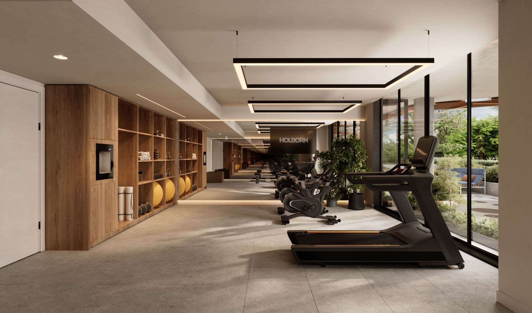 Little Mountain – Fitness corridor with cardio machines, a wall of shelving stocked with exercise balls and mats, a wall-mounted TV, and glass doors opening to an outdoor patio with trees.