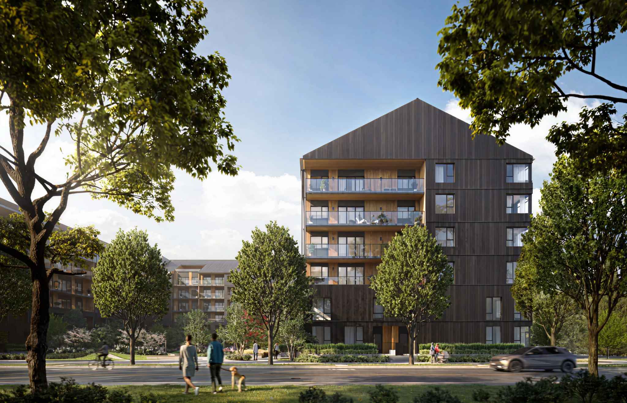 Portwood – A modern mid-rise residential building features dark vertical timber cladding, a gabled roofline, and warm wood-lined balconies with glass railings. Set under a bright daytime sky, lush leafy trees frame the view across a street where pedestrians walk a dog along the sidewalk.