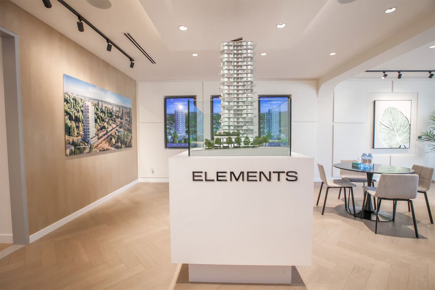 Elements – Sales presentation centre interior featuring an illuminated architectural model of the Elements tower on a pedestal, aerial renderings on the wall, and a display table.