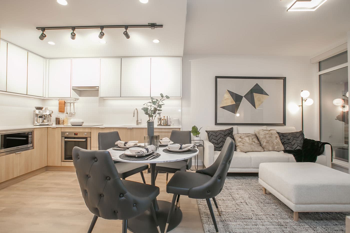 Elements – Open-plan kitchen, dining table set for a meal, and living room with a white sofa, faux-fur pillows and geometric wall art.