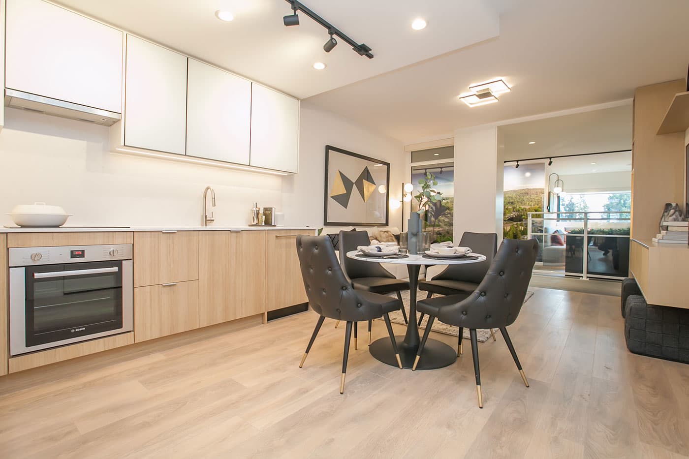 Elements – Kitchen with white upper cabinets, light wood lower cabinets, a built-in wall oven, and a small round dining table nearby.