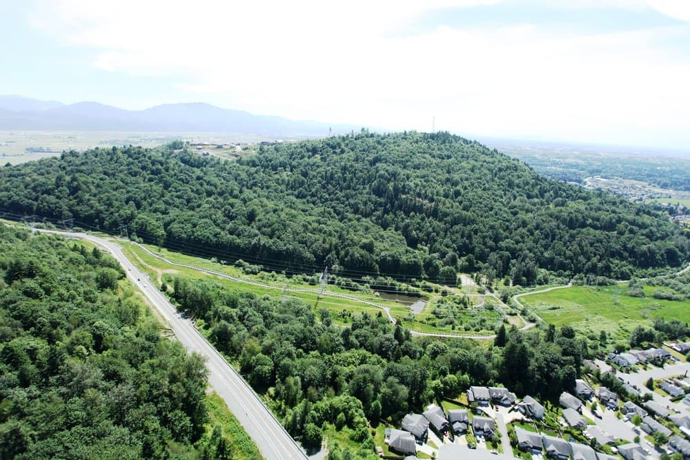 Vicarro – Aerial drone view of a highway and power lines cutting through forested land, with farmland in the valley beyond.