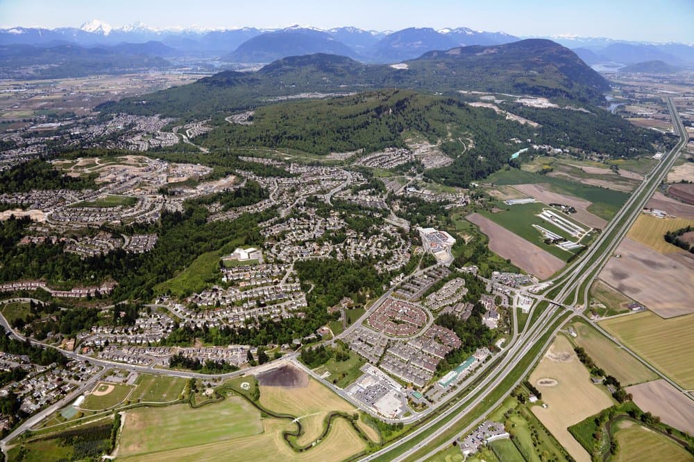 Vicarro – Aerial drone view over a mixed residential and farming valley with snow-capped mountains in the distance.
