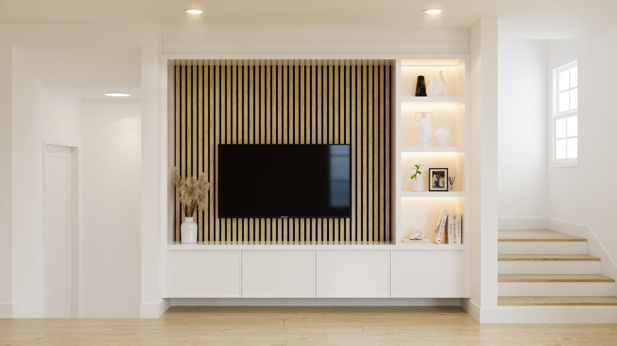 Fiore – A modern living room feature wall featuring a wall-mounted flat-screen television set against vertical wood slat accent panels, flanked by illuminated open shelving with decorative objects. White built-in cabinetry sits below the TV, complement light wood flooring and a adjoining staircase in a bright, minimalist interior space.